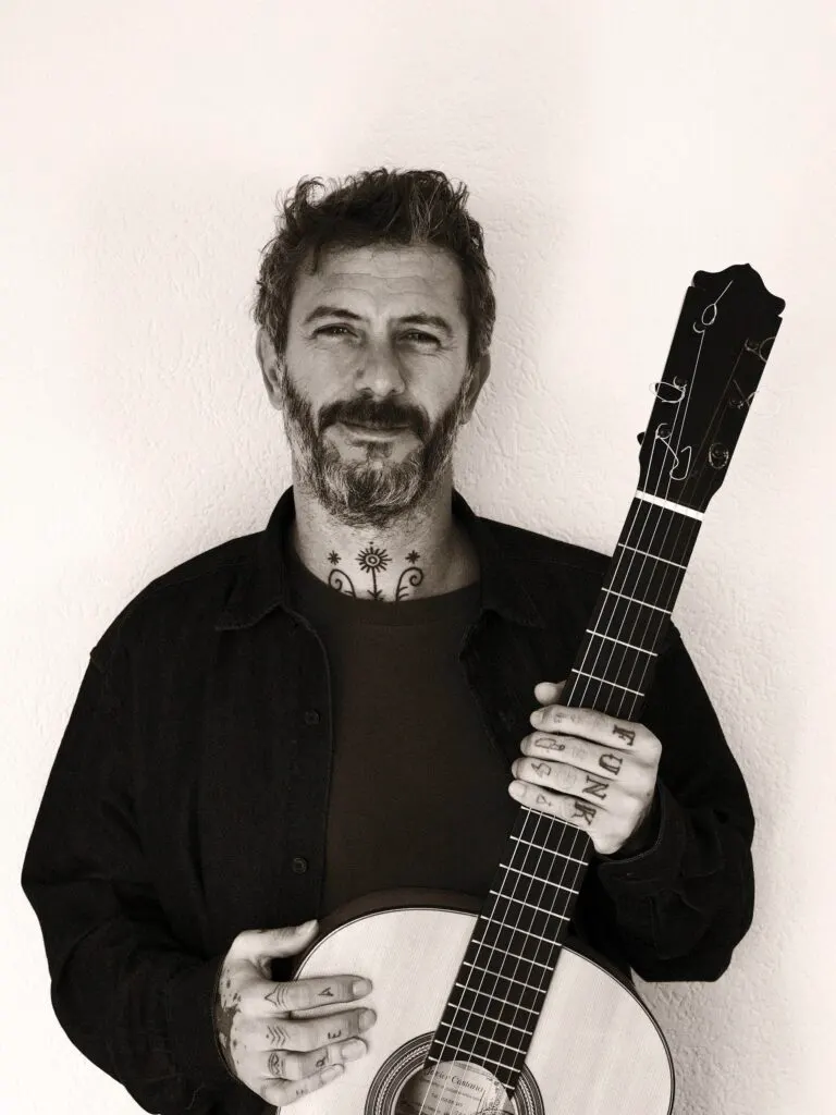 Juan Medina sentado con la guitarra flamenca sobre la pierna, mirando al frente